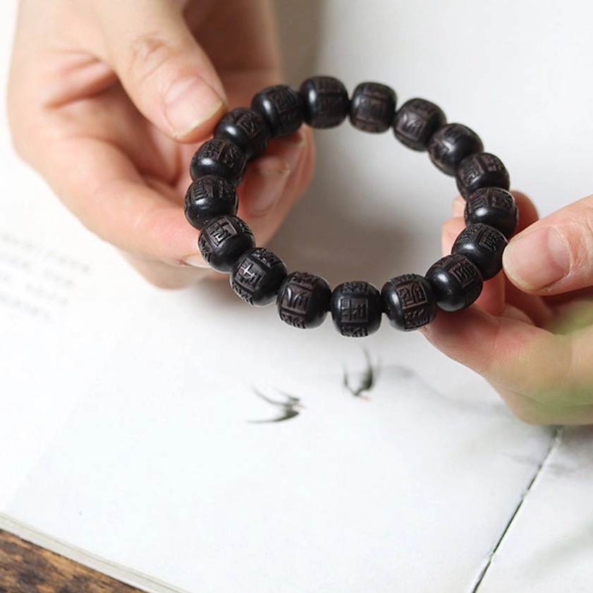 Dark wooden prayer bead bracelet laid on book page showing natural wood grain and carved script detail