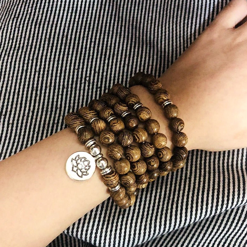 Woman wearing layered wooden Buddhist mala bracelet with lotus charm on wrist, spiritual meditation jewelry