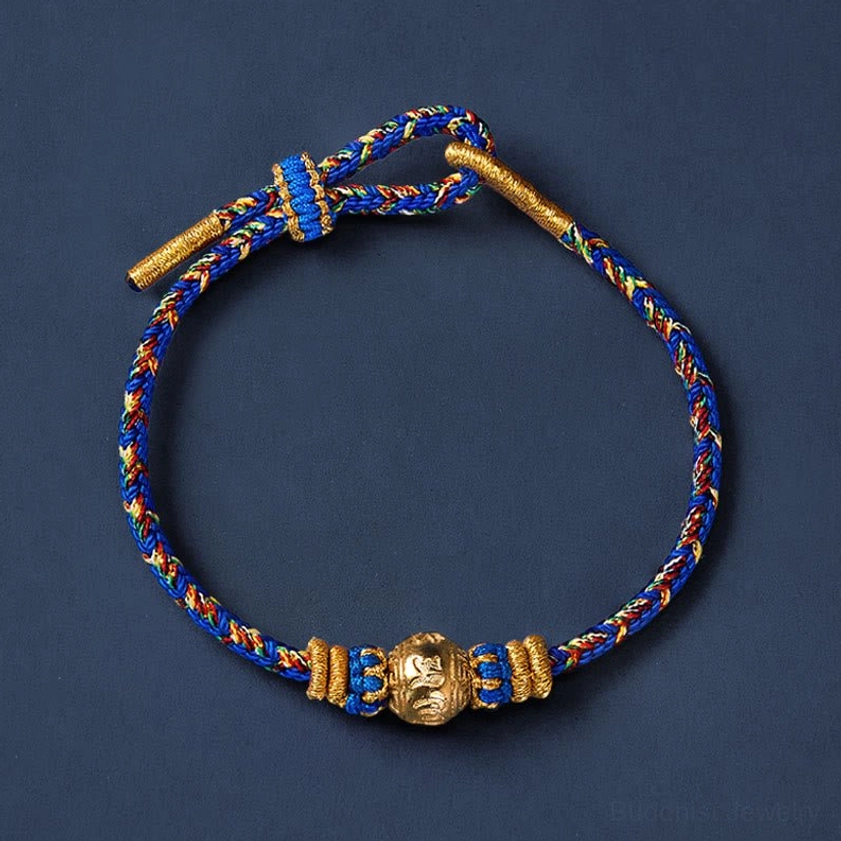 Minimalist woven Buddhist bracelet with blue-gold braided cord and toggle fastener on dark background