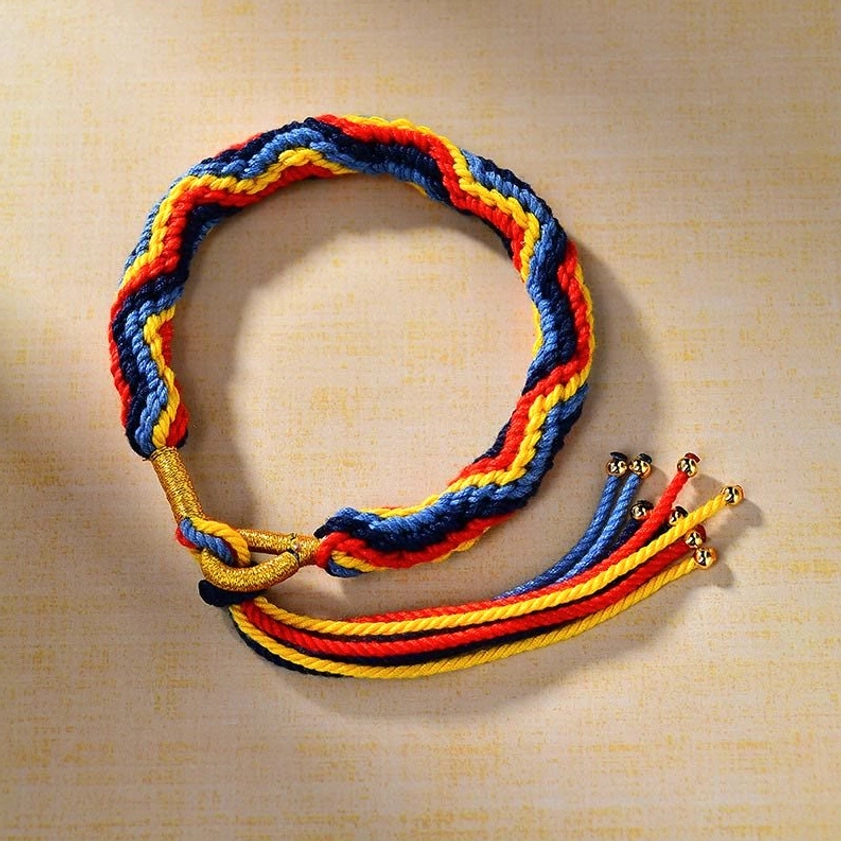 Top-down flat lay of circular woven Buddhist bracelet featuring multiple beaded tassels and gold clasp closure on light tan fabric background