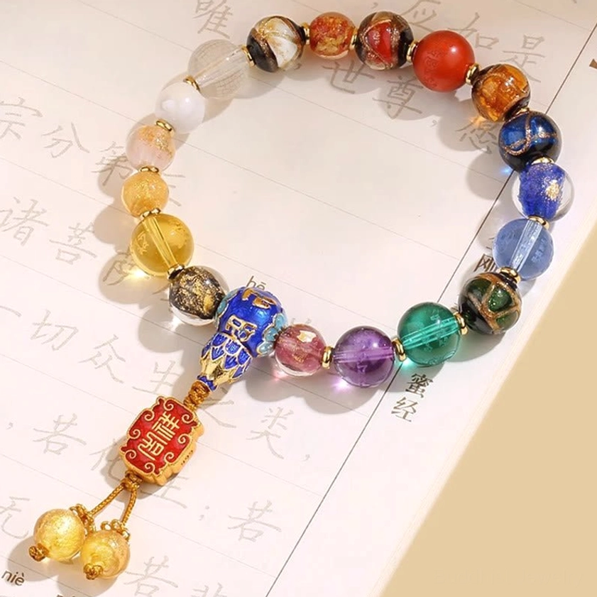 Handcrafted Buddhist wrist mala with mixed color gemstone beads, red enamel pendant, and golden bell charms on calligraphy paper background