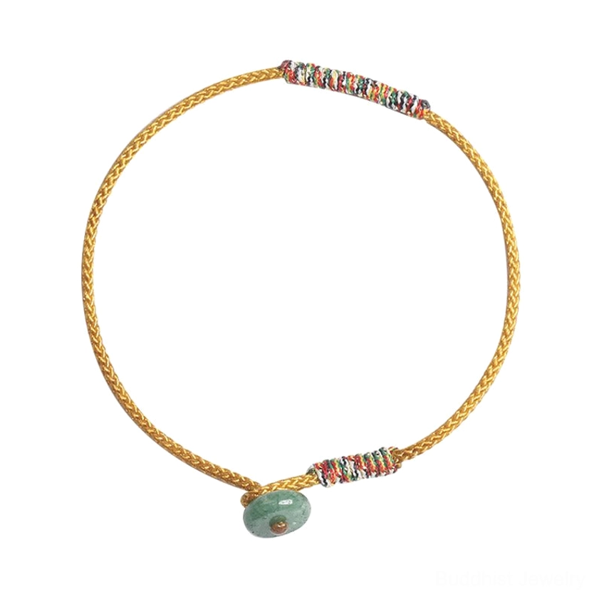 Yellow braided Buddhist luck bracelet with dual woven trim sections and green aventurine charm, flat lay product photography