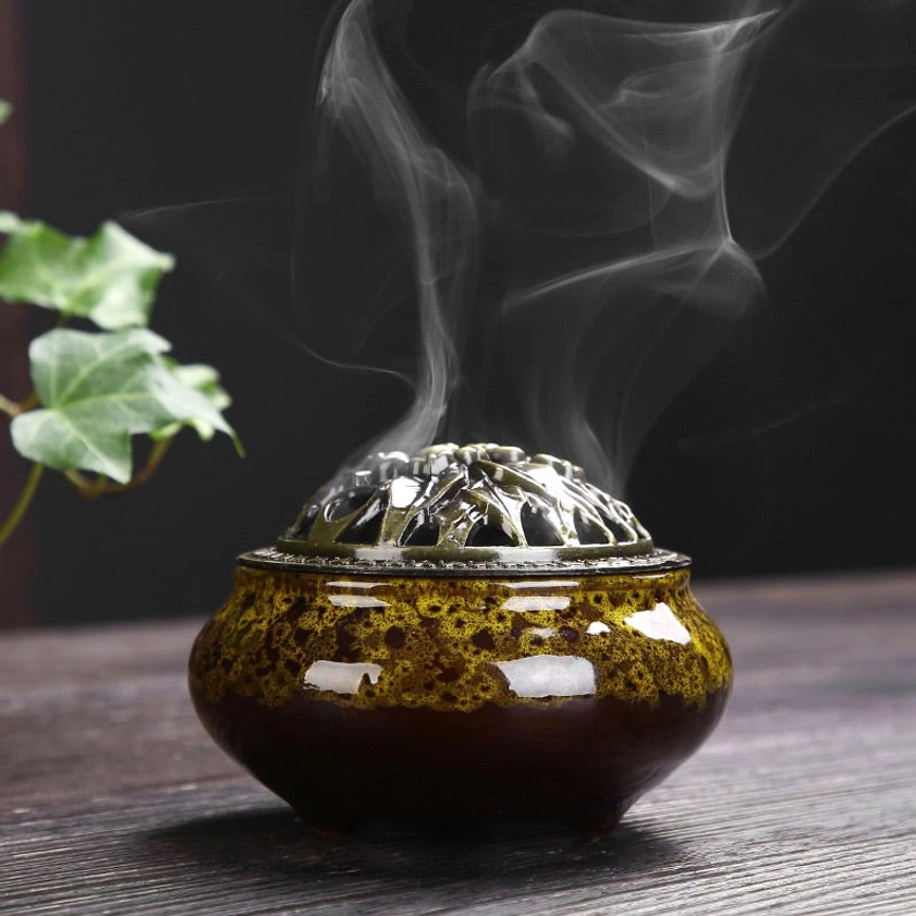 Yellow-brown glossy glazed ceramic incense burner with bronze floral lid emitting fragrant smoke