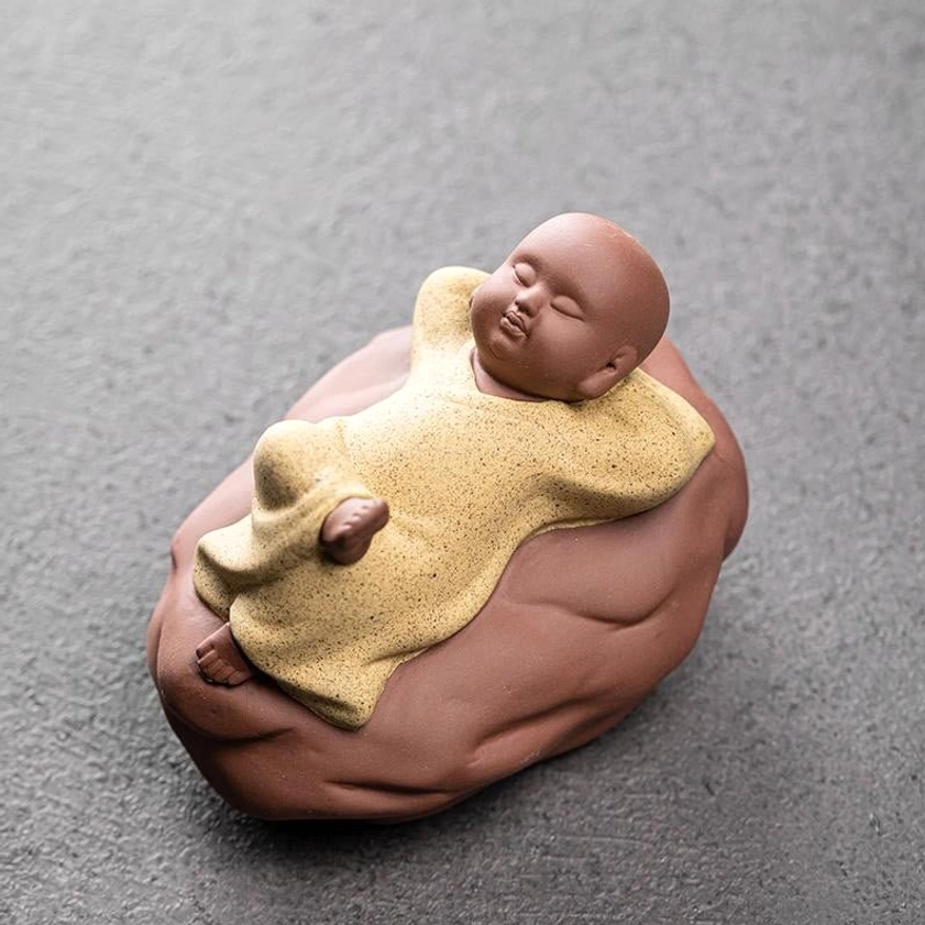 Yellow ceramic resting monk statue in peaceful reclining pose on brown base, studio view