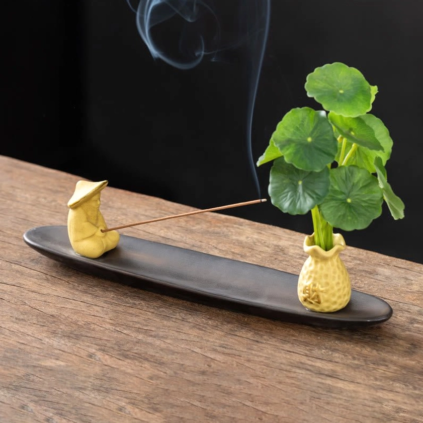 Yellow Fisherman Buddhist incense holder with figurine, vase, and penny grass with curling incense smoke