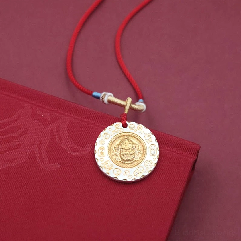 Yellow Jambhala pendant necklace with clear embossed deity design, gold and white two-tone finish on red braided rope with blue-white decorative knots