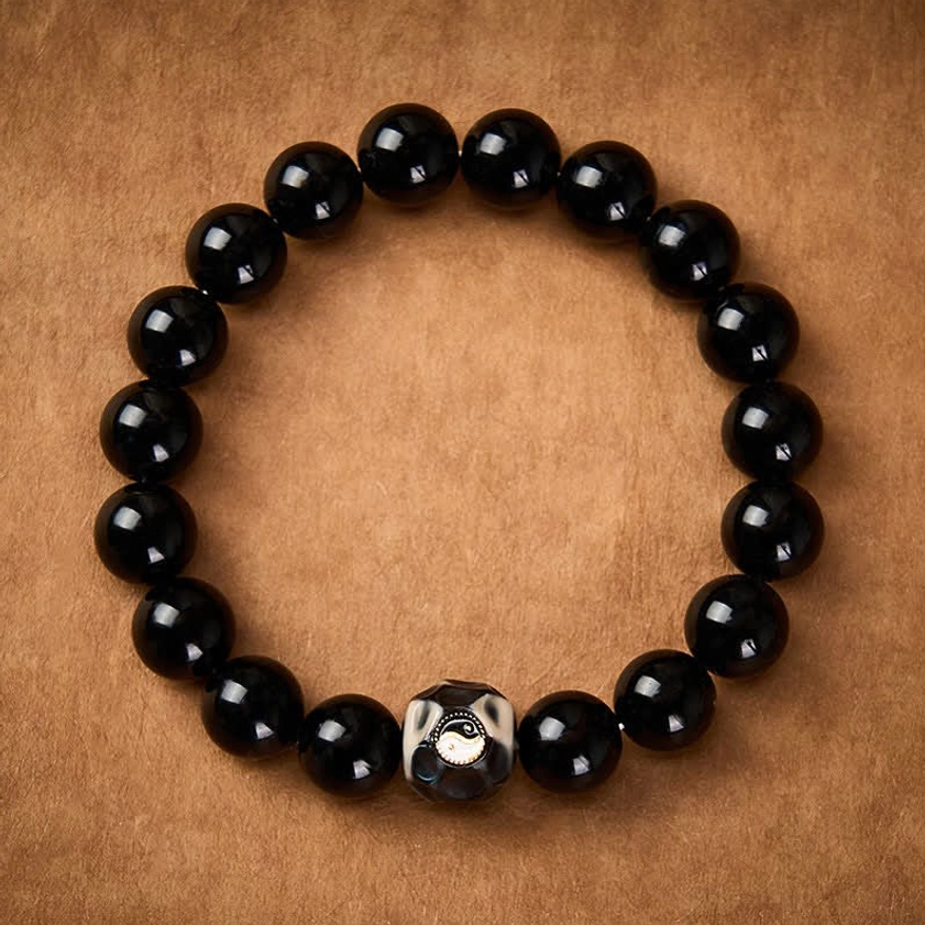 Handcrafted Yin Yang protection bracelet featuring glossy black onyx beads and metallic-trimmed accent bead on leather surface