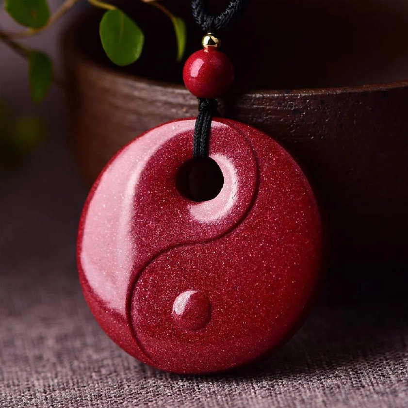 Yin Yang cinnabar pendant necklace with round Tai Chi carving on wine-red granular stone displayed on ceramic tabletop