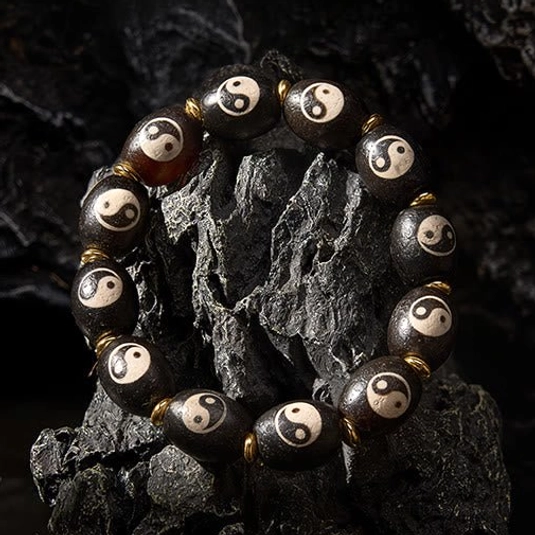 Buddhist yin yang dzi bead bracelet on black stone background oblique angle showcasing agate beads and gold spacers