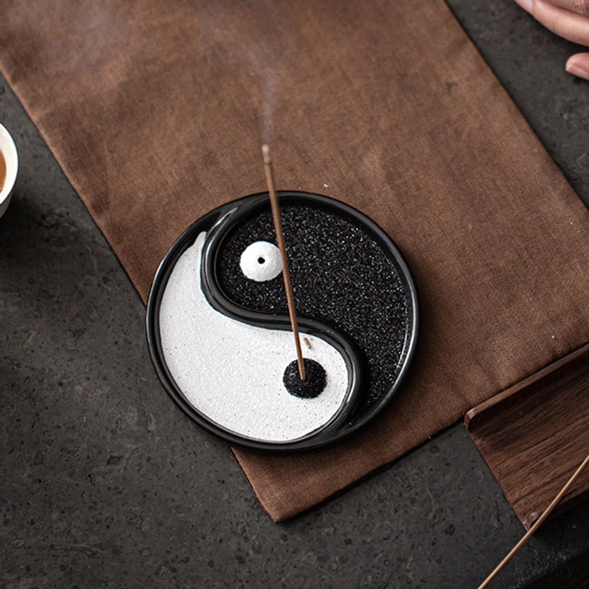 Yin Yang incense holder overhead flat lay with lit incense stick producing gentle curling smoke on brown placemat