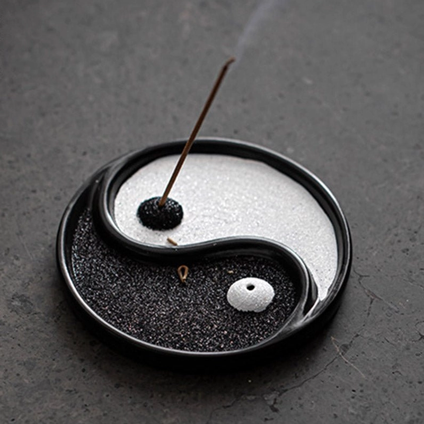 Round yin yang ceramic incense holder close-up overhead view showing black and white sand texture and glossy ceramic border