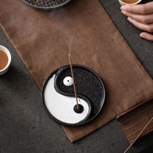 Yin Yang ceramic incense holder flat lay overhead view on tea table with tea cups, black and white sand-filled design