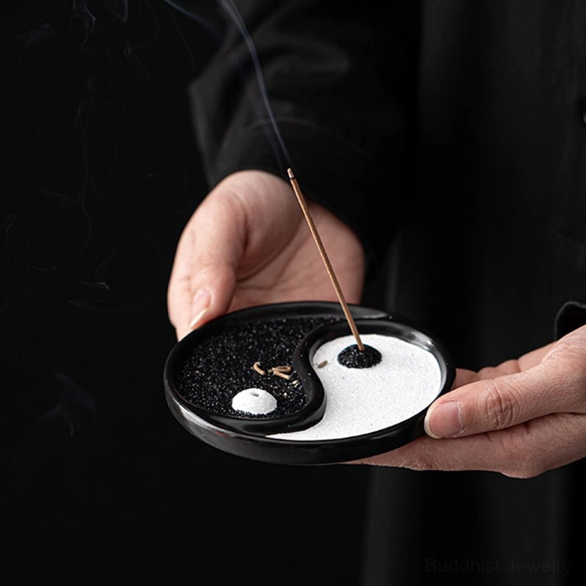 Yin Yang ceramic incense holder being held by two hands for product display against dark indoor background