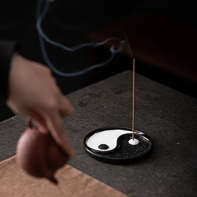 Side eye-level view of yin yang incense holder with curling incense smoke and Yixing teapot on dark table