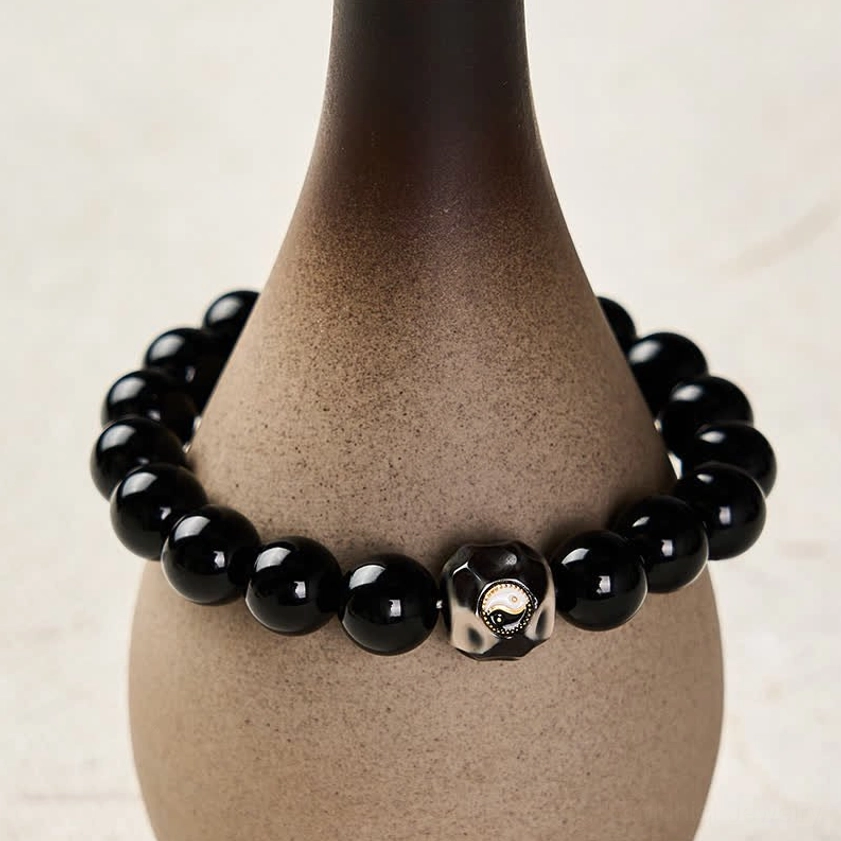 Black Onyx Yin Yang bracelet eye-level side view showing glossy round beads and engraved centerpiece with ceramic prop styling