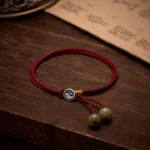 Handmade 925 sterling silver Yin Yang red string bracelet with adjustable cord and green stone beads, displayed on dark wood with ancient Buddhist calligraphy