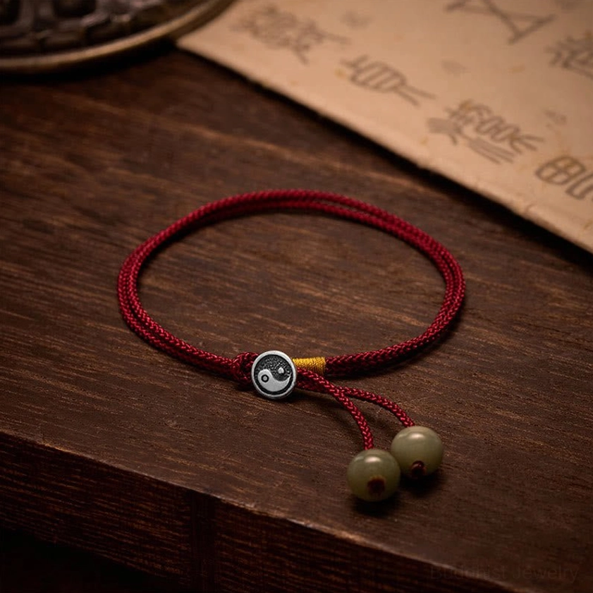 Handmade 925 sterling silver Yin Yang red string bracelet with adjustable cord and green stone beads, displayed on dark wood with ancient Buddhist calligraphy