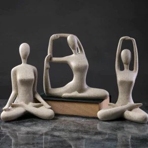 Three abstract yoga meditation female figurines in beige speckled resin with various poses displayed on marble desk with book prop