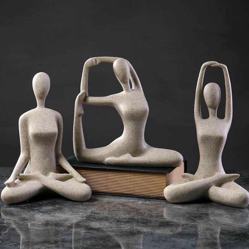 Three abstract yoga meditation female figurines in beige speckled resin with various poses displayed on marble desk with book prop