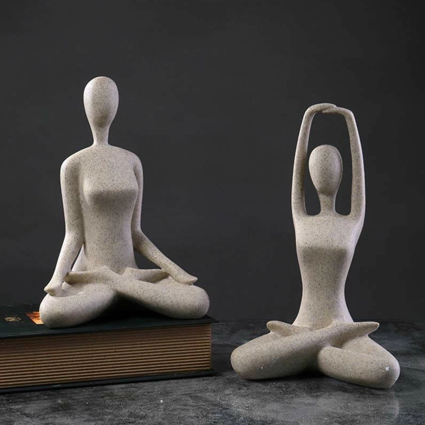 Two abstract yoga meditation female figurines with beige speckled finish displayed on marble desk with book prop