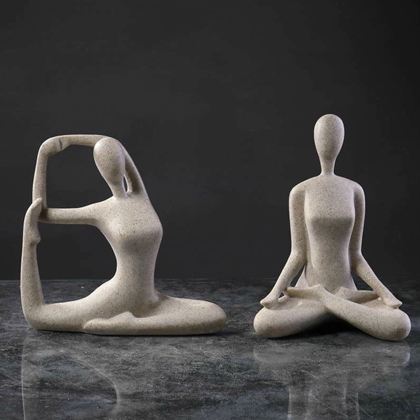 Two abstract yoga meditation female statues in beige speckled resin with mixed poses on dark marble desk backdrop