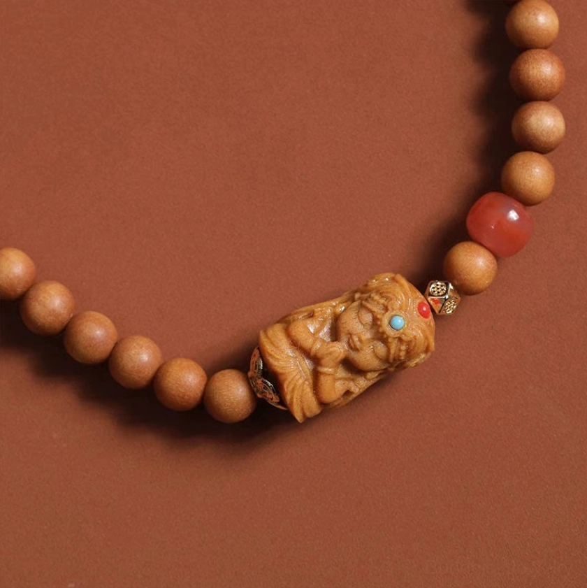 Close-up detail of Zakiram Buddhist wealth bracelet showing carved deity pendant and Red Agate bead from side angle