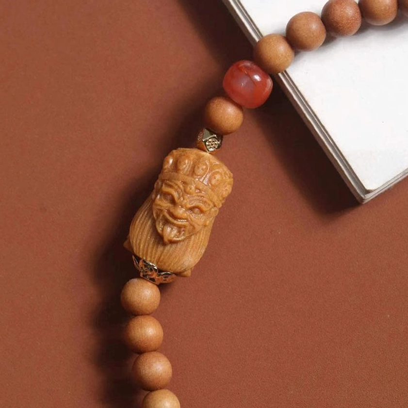 Zakiram wealth bracelet close-up featuring carved deity ornament and metal connector hardware on sandalwood beads