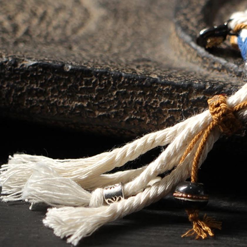 Detailed close-up of bracelet tassel and pendant accessories showing white cotton tassels, tan binding knot, and metal copper charms