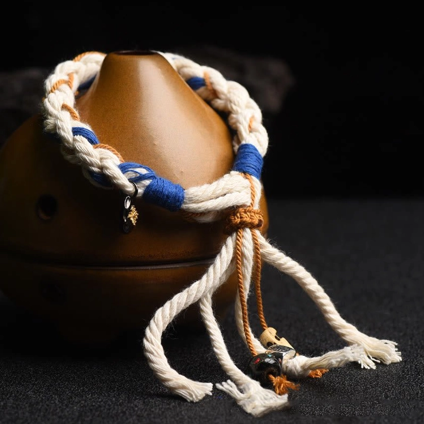 Zakiram string bracelet wrapped on brown ceramic ornament showing braided cotton rope and blue binding details with decorative pendants