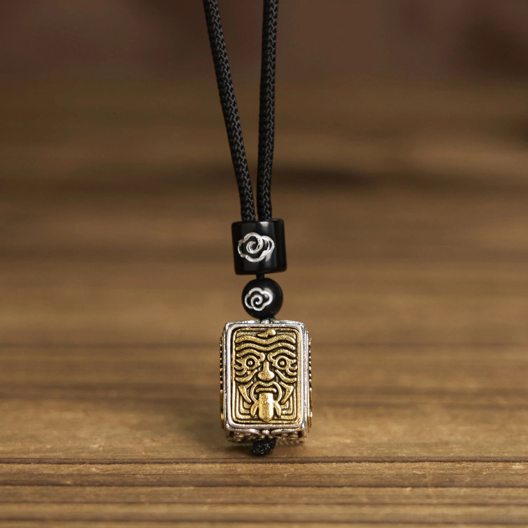 Buddhist Zakiram protection pendant with embossed deity face and cloud-pattern beads, flat lay wooden surface