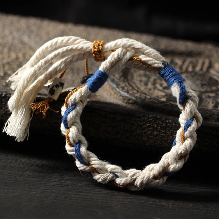 Handmade Zakiram wealth bracelet in tri-color woven pattern displayed on dark wooden surface with blue fabric wraps and loose tassels