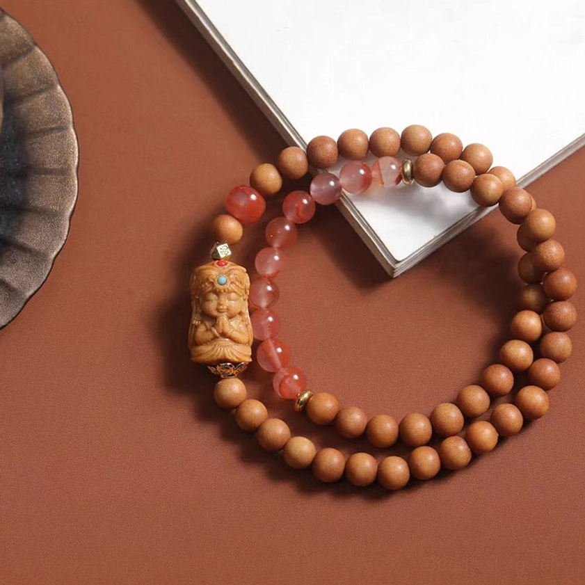 Zakiram Goddess wealth bracelet handmade sandalwood South Red Agate beads with carved deity charm pendant on brown surface