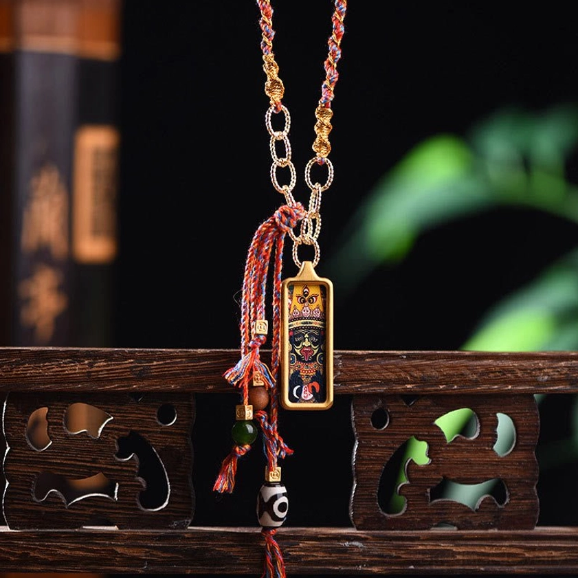 Tibetan wealth deity thangka necklace with red braided tassel, gold chain and dzi bead on carved wooden desk