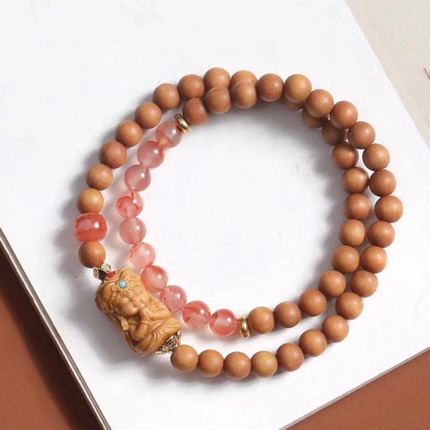 Double-loop Zakiram Buddhist prayer bracelet featuring pink South Red Agate segments and sacred deity pendant on white paper