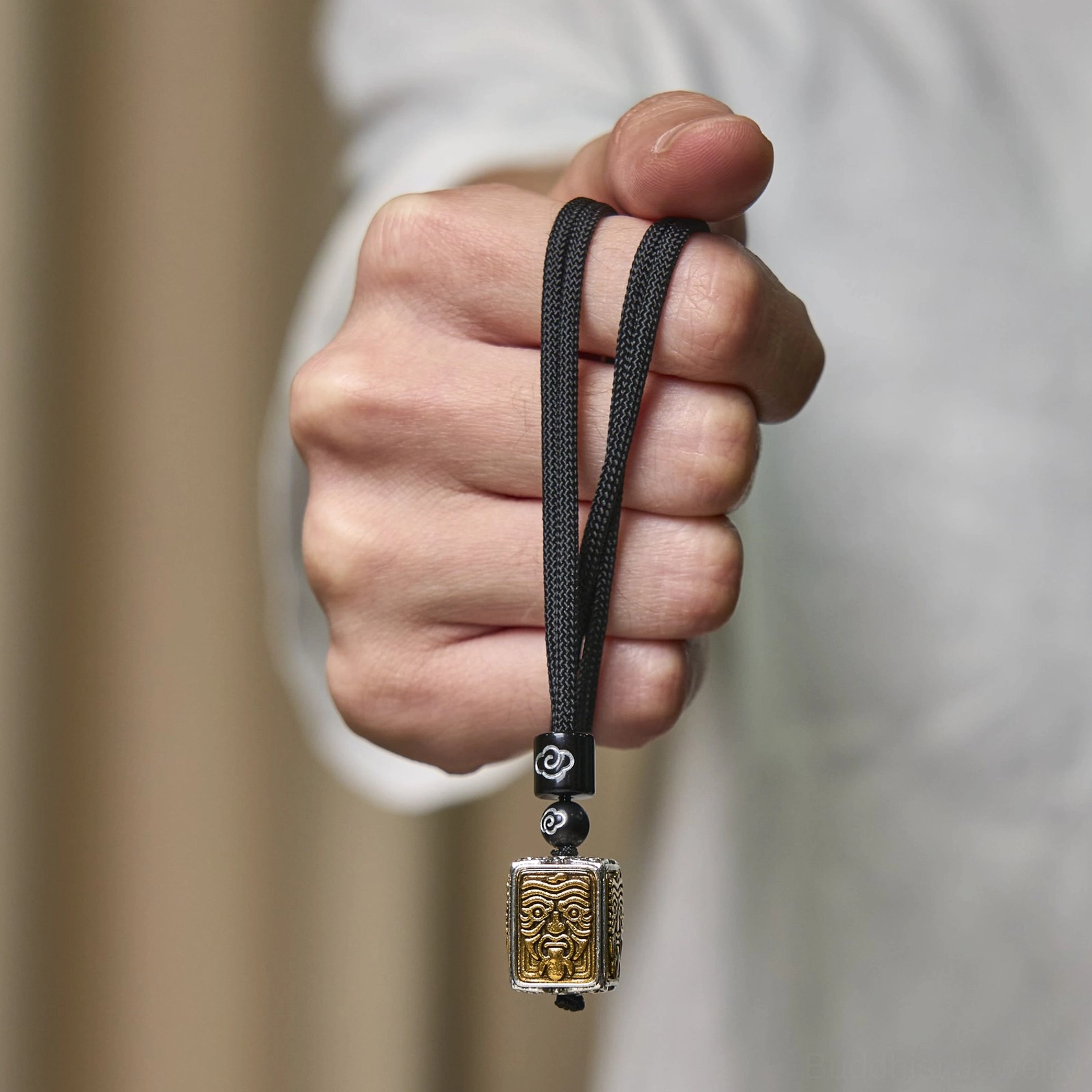 Hand holding Zakiram Buddhist protection pendant necklace with woven lanyard, wearable demonstration