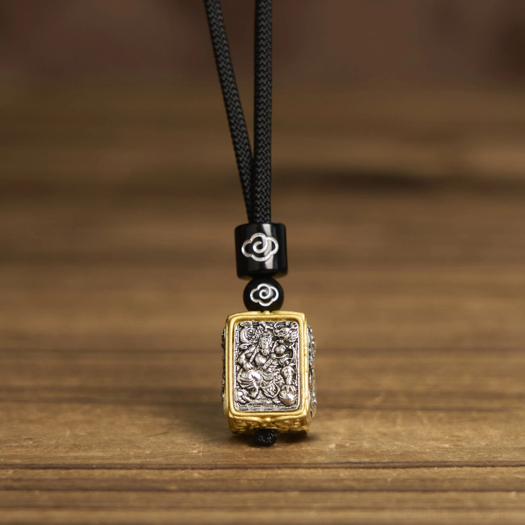 Square Buddhist protection pendant with black braided rope and cloud decoration, top-down view