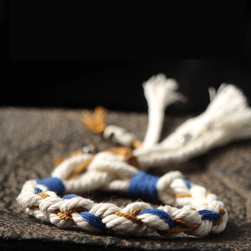 Zakiram prosperity bracelet hanging vertically showing three-color woven rope and hanging charms against dark wooden backdrop