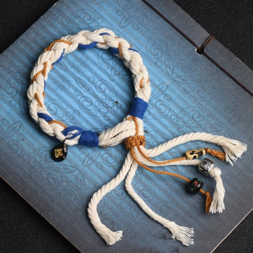 Zakiram Goddess of Wealth handmade string bracelet with multi-color woven rope and decorative pendants, displayed on vintage blue notebook