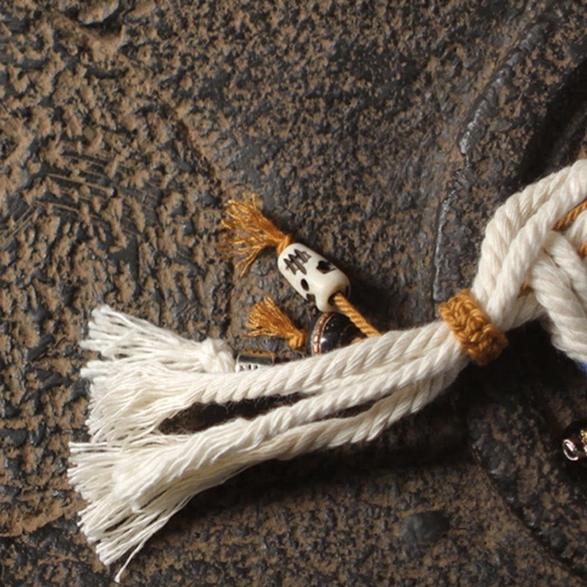 Zakiram prosperity bracelet pendant and frayed tassel details on vintage stone background with decorative metal accents and woven binding