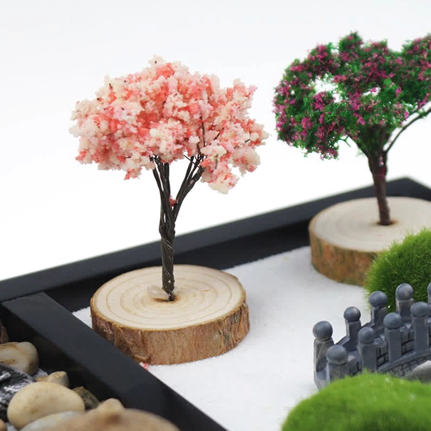 Zen meditation garden close-up with pink blossom tree, wooden base, and mini stone bridge