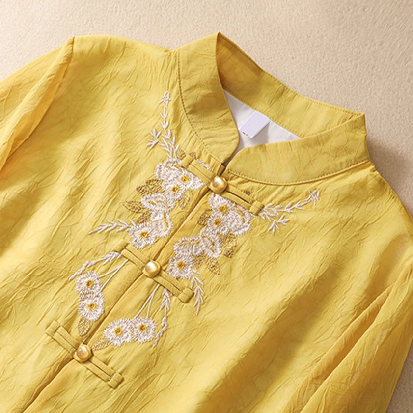 Close-up detail of yellow tunic top showing traditional frog button closures with bead details and white floral embroidery on crinkled fabric