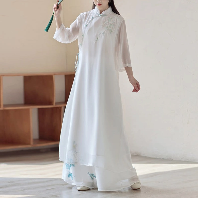 Spiritual practice cheongsam dress and wide leg pants ensemble, front-side angle with model holding green tassel accessory and displaying embroidered floral details