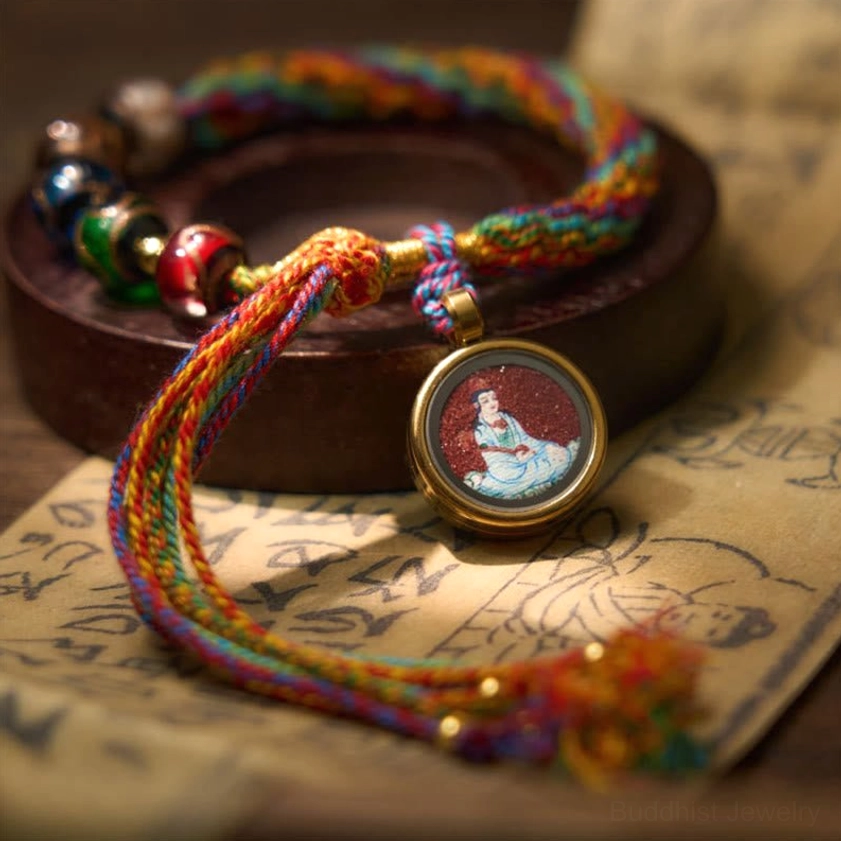 Zodiac blessing string bracelet displayed on vintage paper and wooden holder, showing multicolor braid detail with glass beads and Buddha pendant