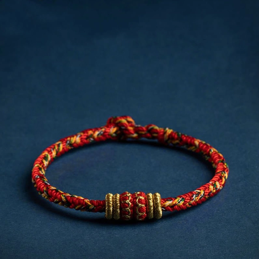 Handmade red braided buddhist zodiac natal buddha string bracelet with gold decorative knots, flat lay view