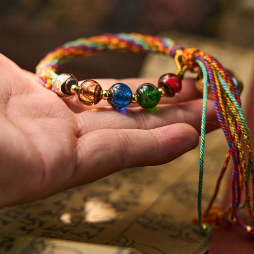 Zodiac natal Buddha bracelet on palm showing colorful glass beads, braided rope construction, and long spiritual tassel ends