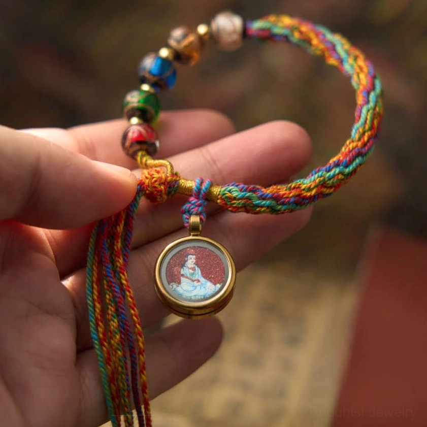 Chinese zodiac natal Buddha cinnabar bracelet front hand-held view displaying cinnabar round pendant with multicolor braided rope and decorative beads