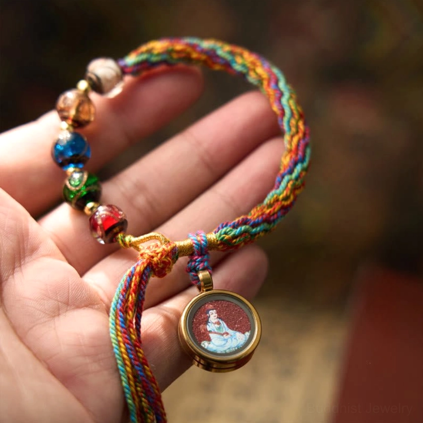 Chinese zodiac natal Buddha cinnabar blessing bracelet displayed on human palm, showing colorful braided silk rope with glazed beads and round metal Buddha pendant